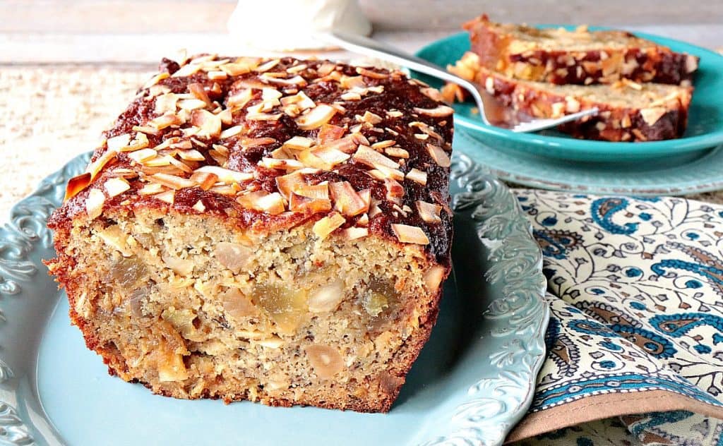 A sliced loaf of Gluten-Free Tropical Quick Bread with candied fruit and coconut on a blue plate.