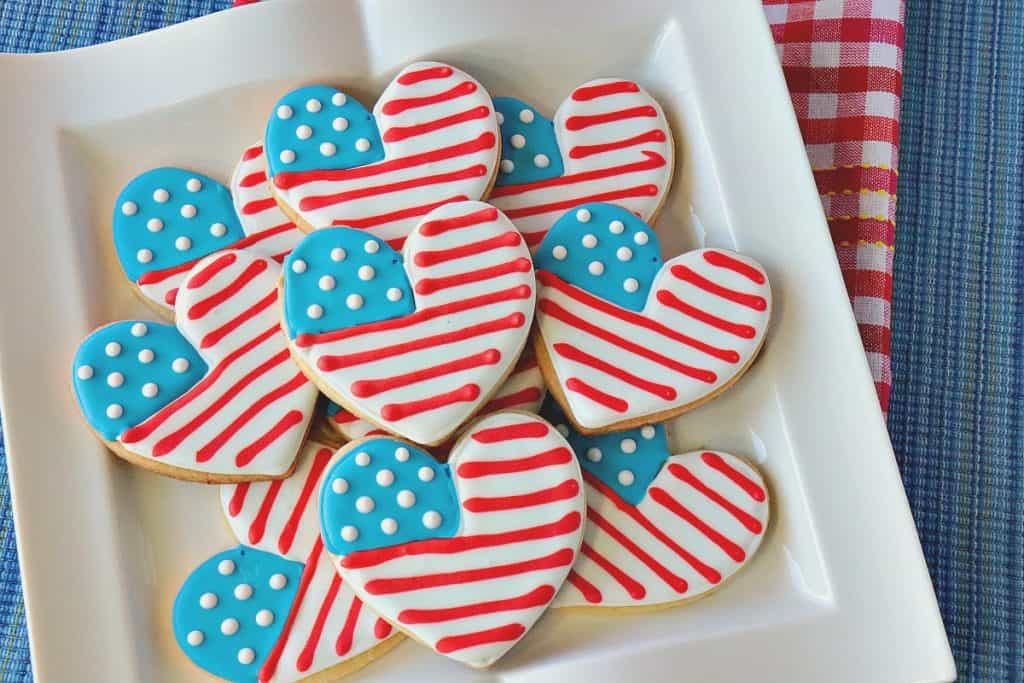 Stack of American flag heart cookies on a square white plate with a red and white checked napkin.