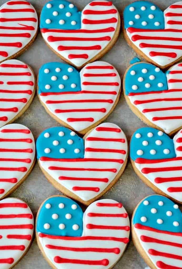Closeup overhead photo of red, white, and blue American Flag Heart decorated sugar cookies on a baking sheet.
