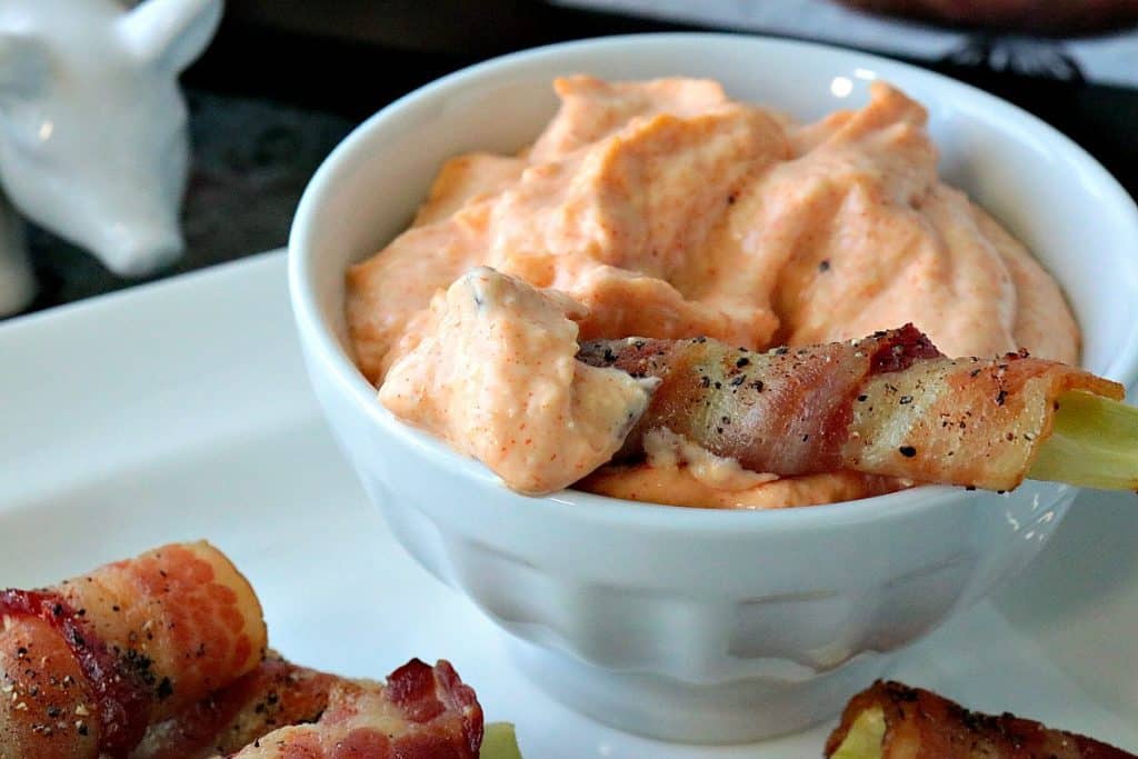 Closeup photo of a bacon wrapped broccoli stem with pepper in a bowl of dipping sauce.