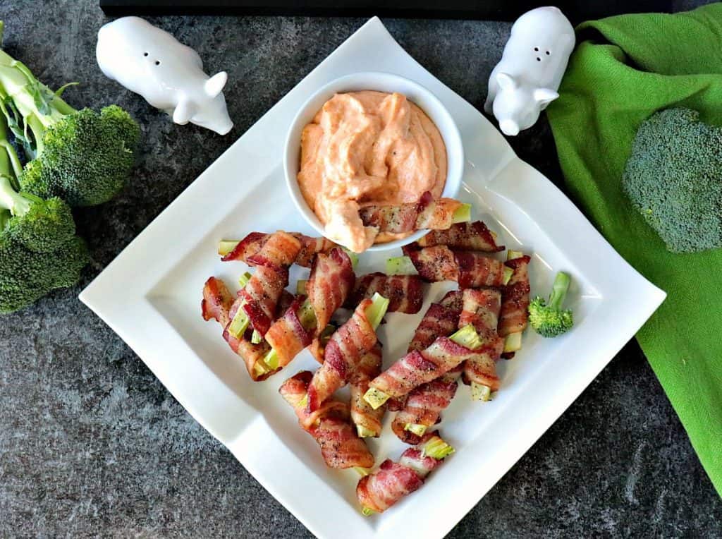 Overhead photo of bacon wrapped broccoli stems on a square plate with dipping sauce in the corner.