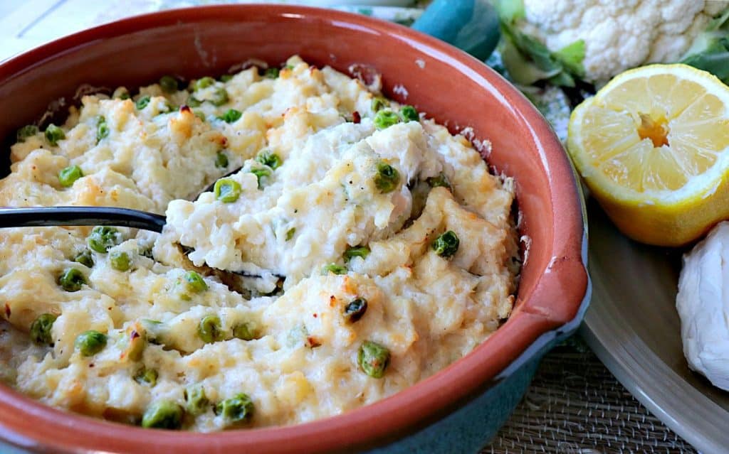Mashed cauliflower casserole in a dish with a spoon and some peas.