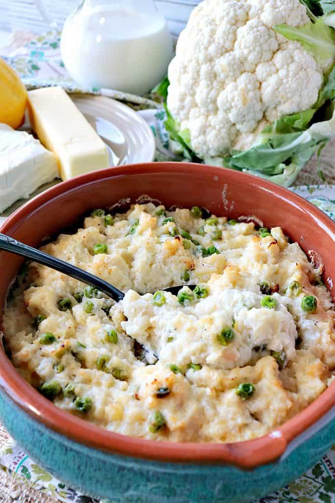 Vertical photo of a cheesy cauliflower casserole with cream, peas, cauliflower, butter, and cream cheese in the background.