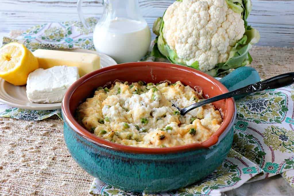 Cheesy Mashed Cauliflower Casserole in a casserole dish with fresh cauliflower, cream, and butter in the background