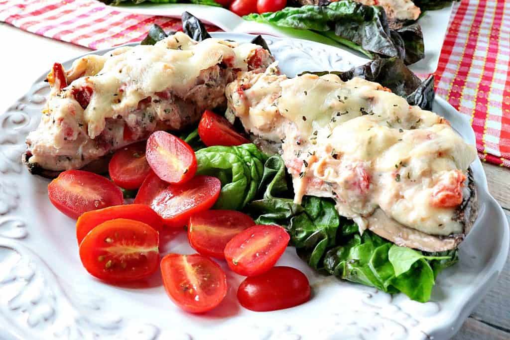 A pretty white plate along with a cut in half Chicken Parmesan Stuffed Portobello mushroom along with lettuce, tomatoes, and melted cheese.