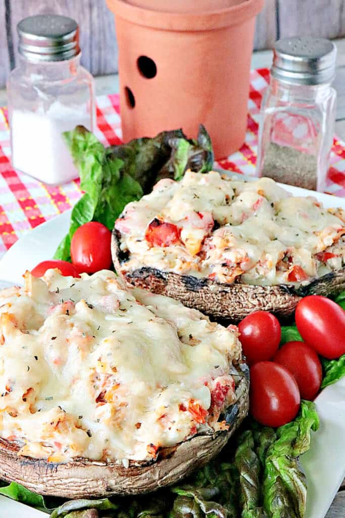 A vertical closeup image of two Chicken Parmesan Stuffed Portobellos on a white plate with lettuce and tomato.