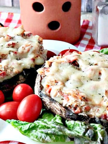 Two Chicken Parmesan Stuffed Portobellos on a plate with lettuce and tomatoes.