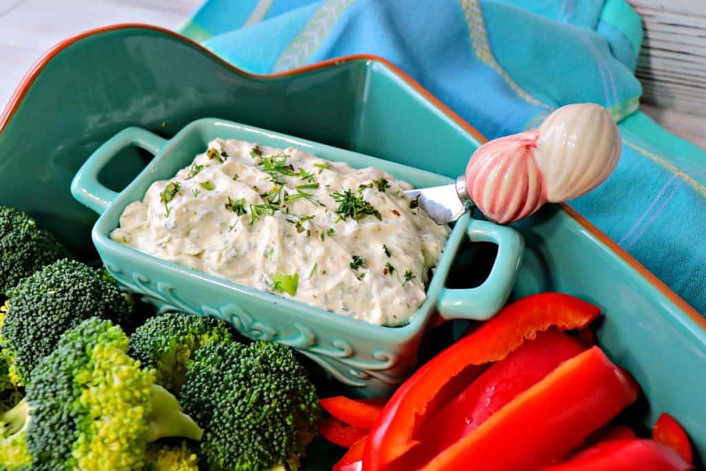 A blue crock filled with Homemade Boursin Cheese and surrounded by fresh vegetables. 