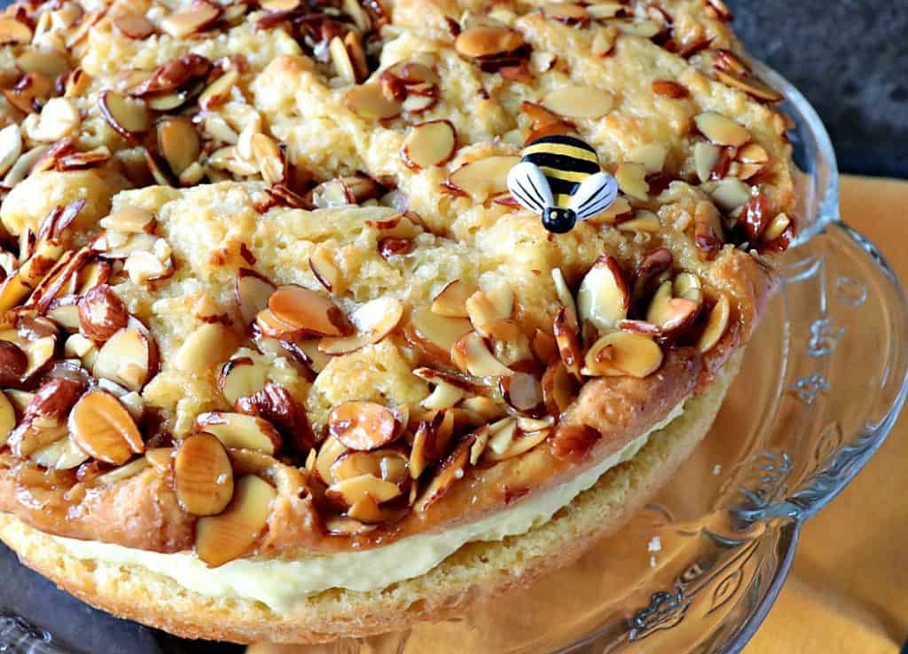 A closeup overhead photo of a German bee sting cake on a glass cake plate with a yellow napkin and a little bee.