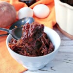 A white bowl filled with a serving of Grated Sweet Potato Pudding and a spoon.