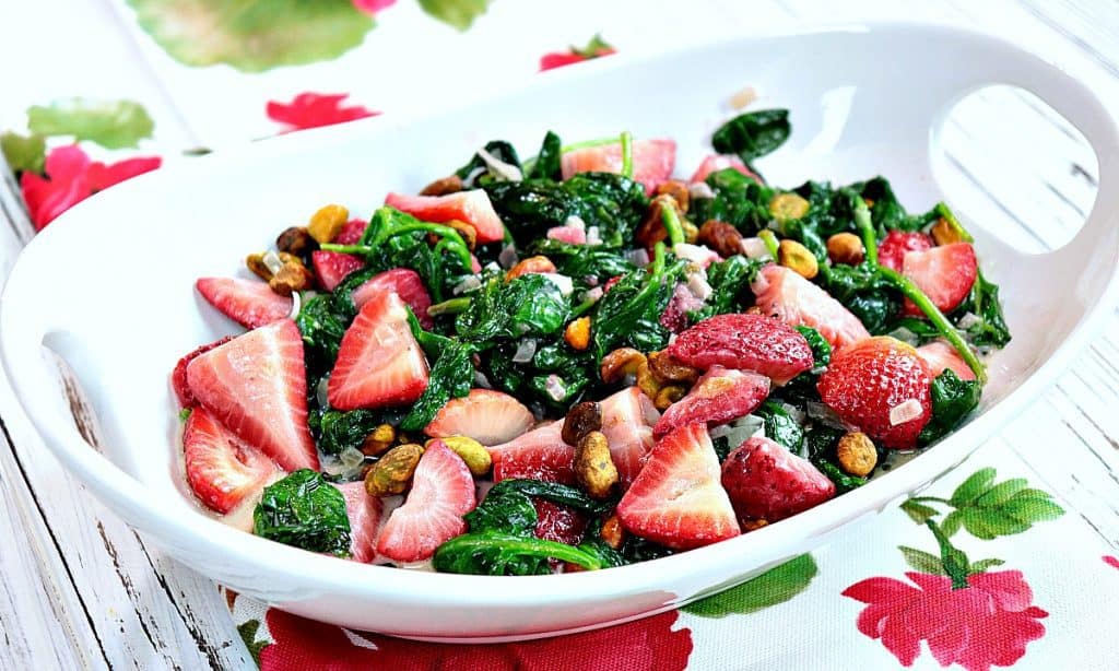 An oval bowl filled with sautéed creamed spinach and strawberries side dish.