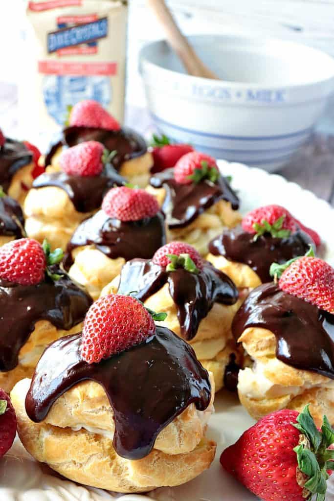 A closeup vertical image of luscious chocolate strawberry cream puffs on a serving platter.