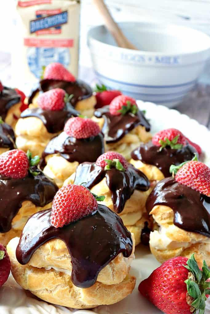 A closeup vertical image of luscious chocolate ganache topped strawberry filled eclairs on a serving platter.