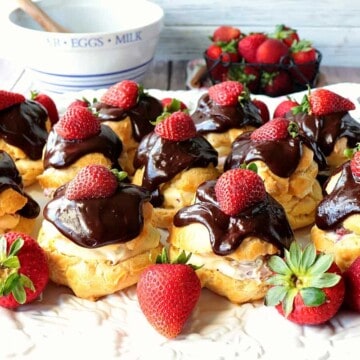 A tray filled with chocolate covered strawberry filled eclairs with fresh strawberries as garnish