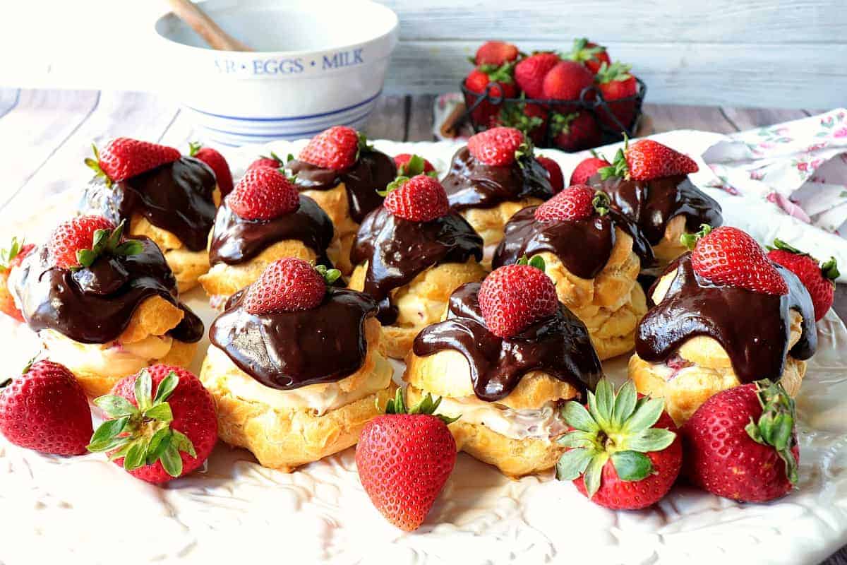 A pretty horizontal photo of a platter of chocolate covered eclairs with strawberries. Elegant chocolate dessert recipes for Valentine's day.