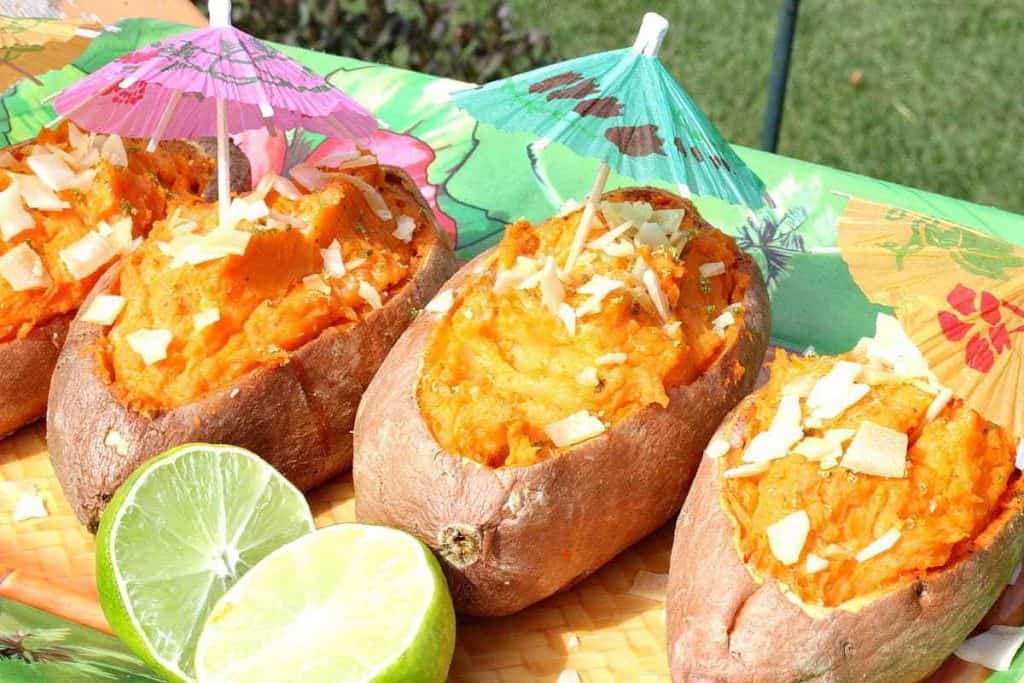 A horizontal photo of 4 tropical stuffed sweet potato boats with party umbrellas and a lime.