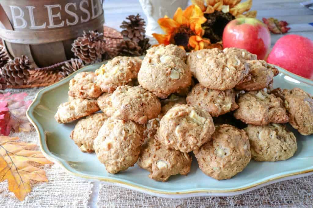 A platter of apple oatmeal cookies with fresh apples in the background and sunflowers
