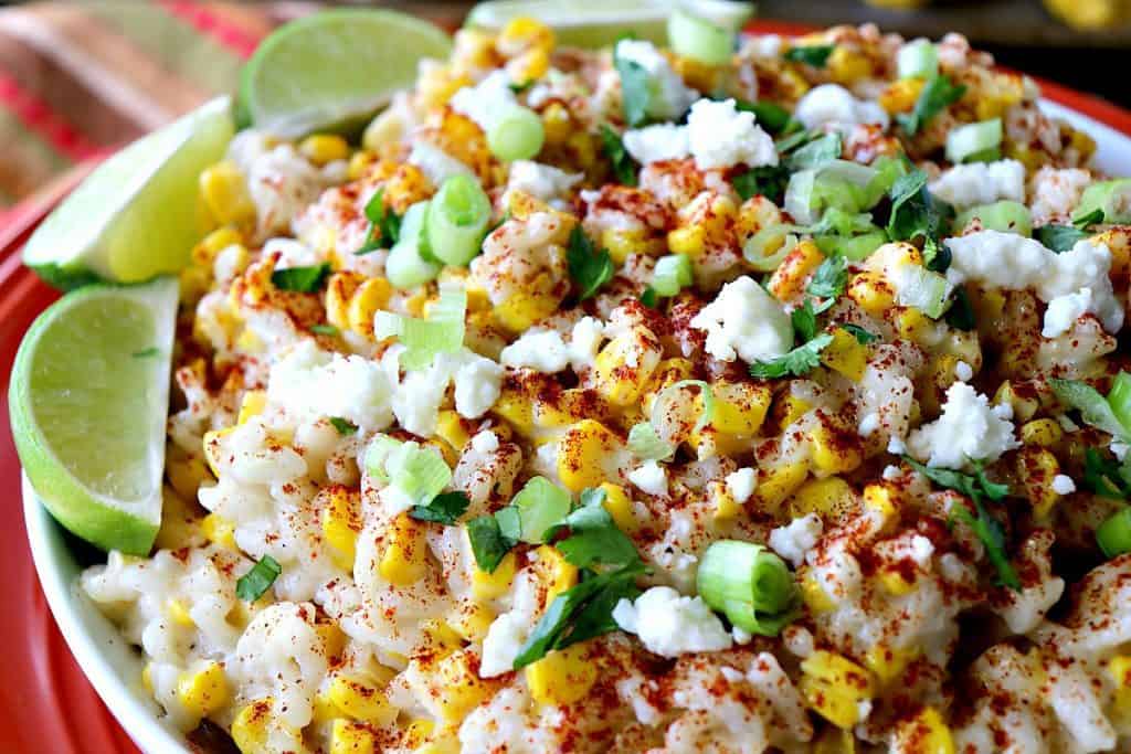 Closeup photo of Mexican street corn risotto with lime wedges, scallions, smoked paprika and cheese.