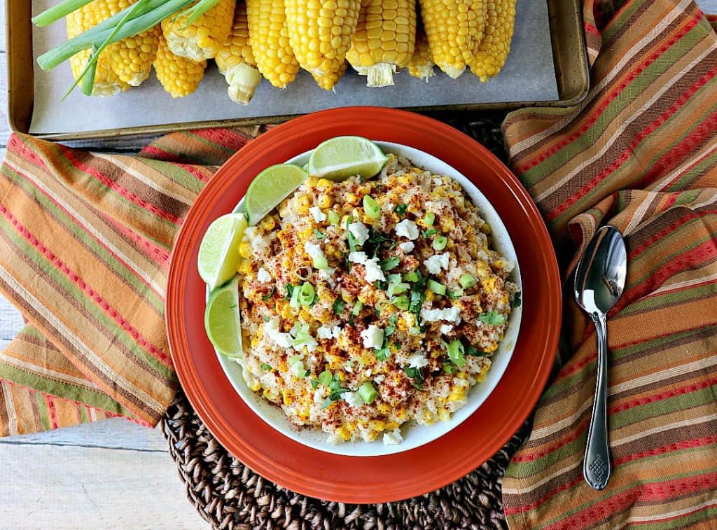 Overhead photo of a bowl of Mexican street corn risotto with a spoon and a tray of corn on the cob.