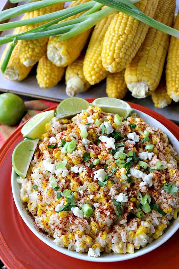 A colorful bowl of Mexican street corn risotto with limes, cheese, scallions and corn on the cob.