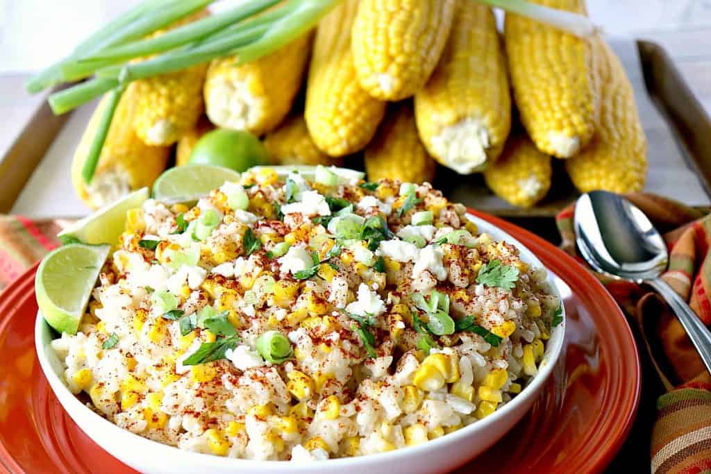 White bowl filled with Mexican street corn risotto and corn on the cob in the background.