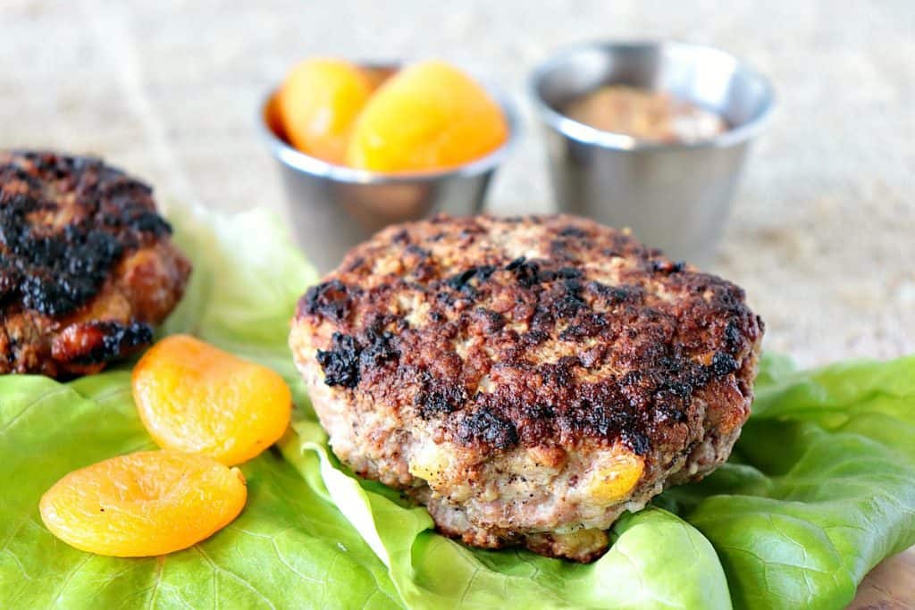 A Pork Burger with Dried Apricots without a bun on lettuce leaves with dried apricots as garnish.