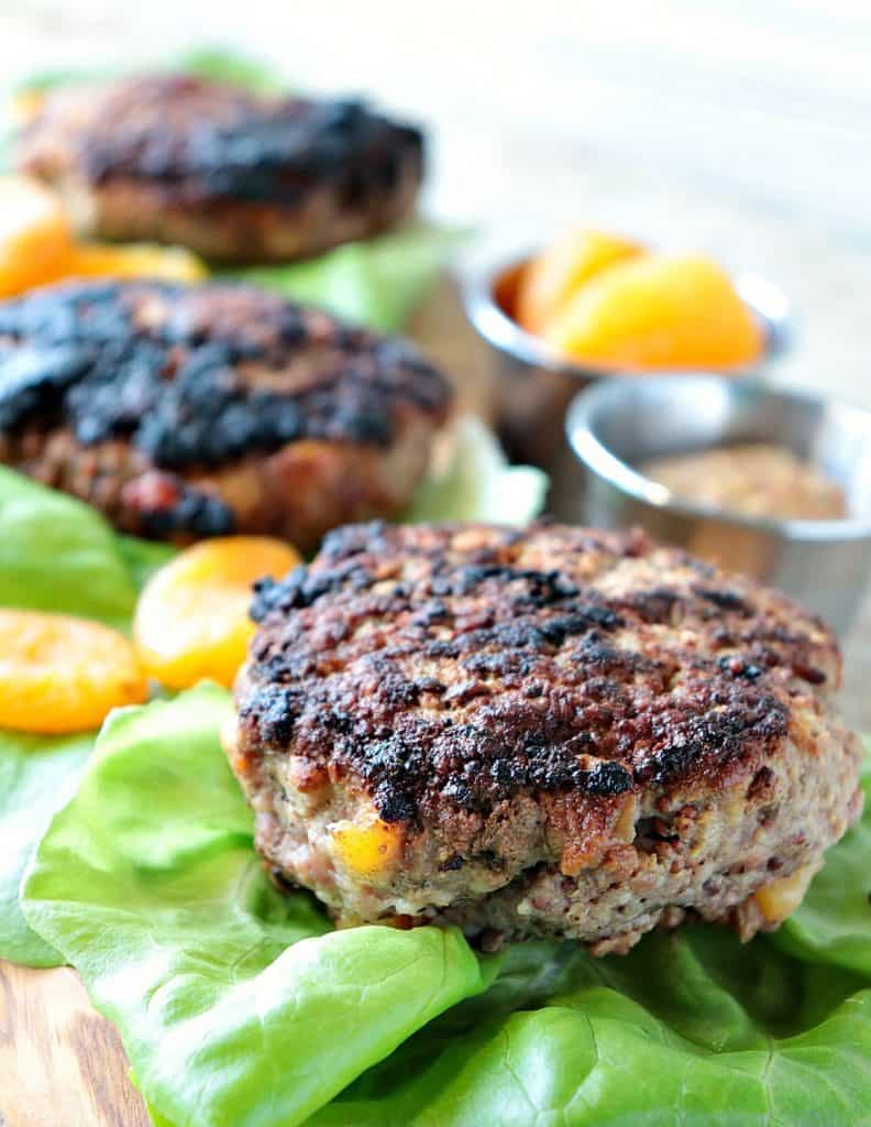 A vertical closeup of a Pork Burger with Dried Apricots along with lettuce leaves and dried apricots as garnish.