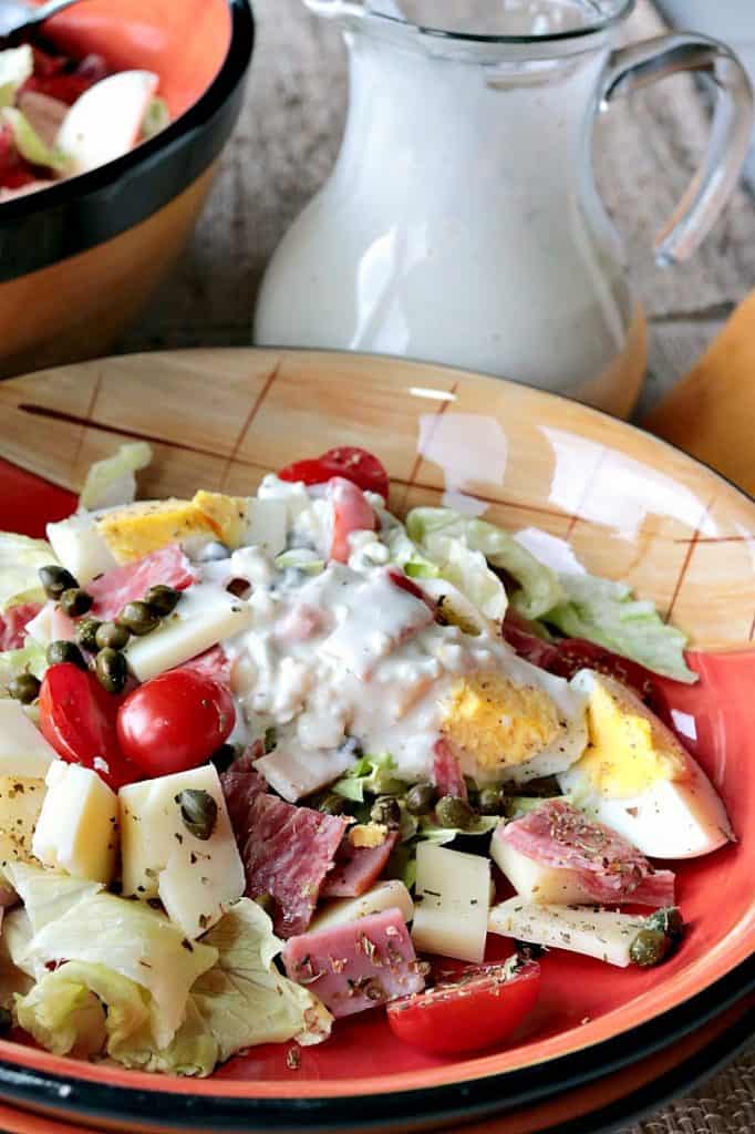 A closeup vertical photo of a chef's salad topped with homemade blue cheese dressing and tomatoes, eggs, meat and cheese