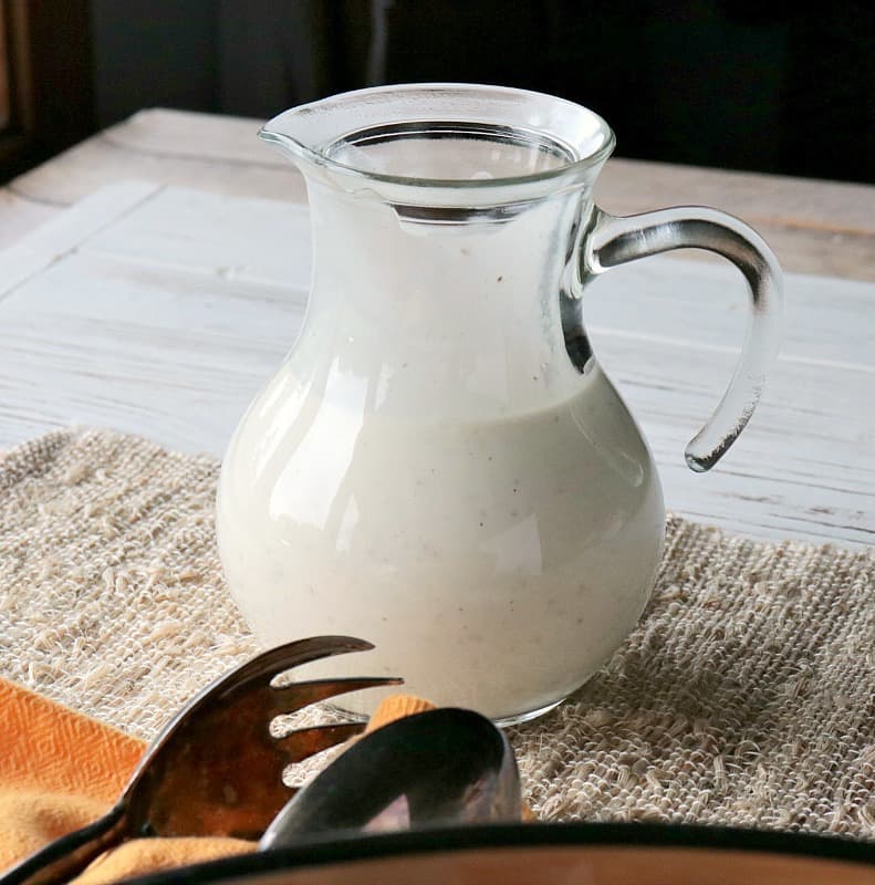 A small glass pitcher of homemade blue cheese dressing.