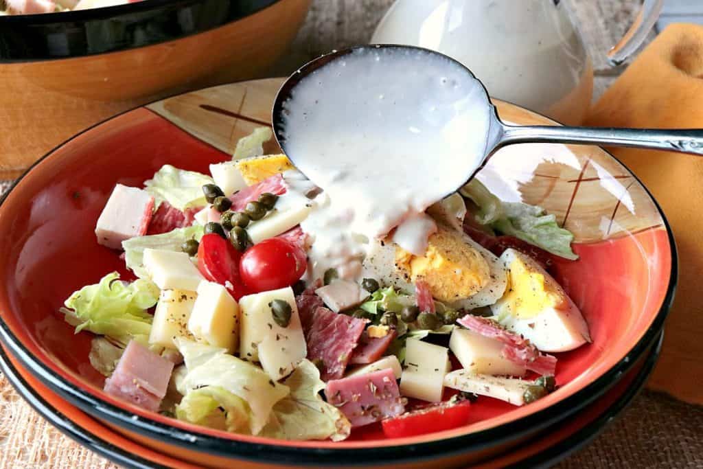 A closeup photo of blue cheese dressing being pored over a chef's salad.