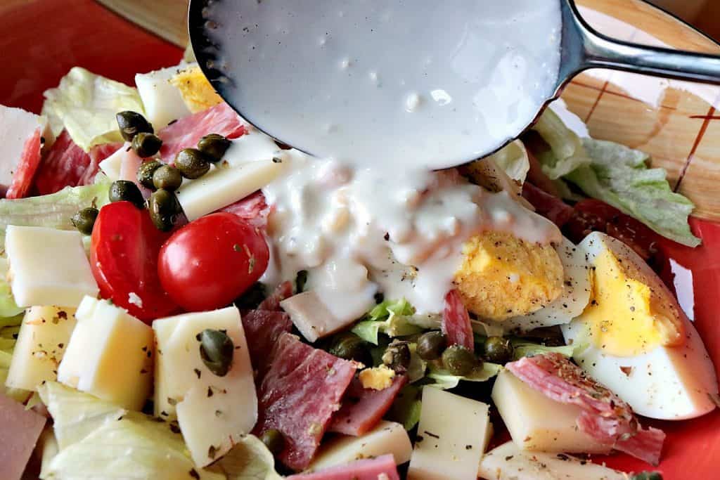 A closeup photo of a salad with meat, cheese, capers, and lettuce with homemade blue cheese dressing.