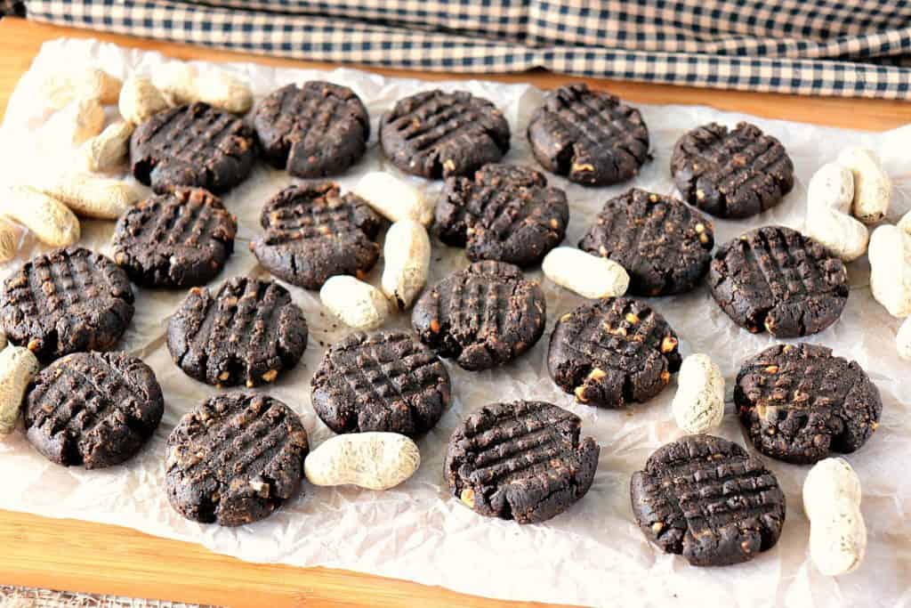 Horizontal photo of a bunch of chocolate peanut butter cookies on a board with peanuts in the shell surrounding them.