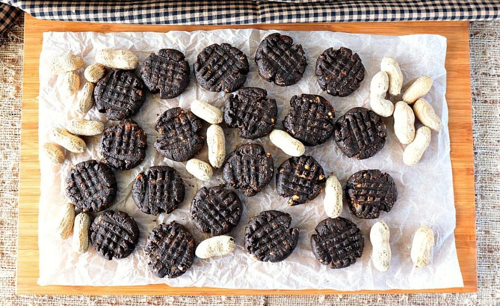 Overhead photo of sugar free chocolate peanut butter cookies on a board with parchment paper and peanuts. 