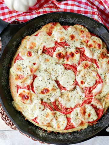 An overhead photo of a Deep Dish Garlic Lover's Pizza in a cast iron skillet with a red and white checkered napkin on the table.