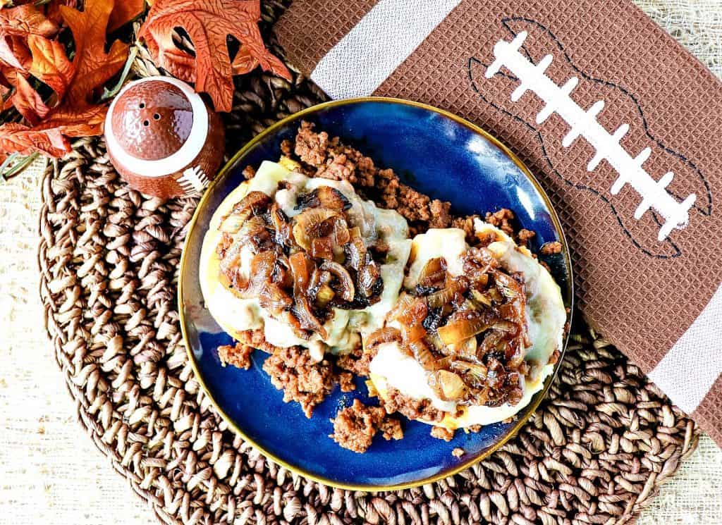 Overhead photo of an open-faced French Onion Sloppy Joes sandwich on a textured place mat and a football napkin.