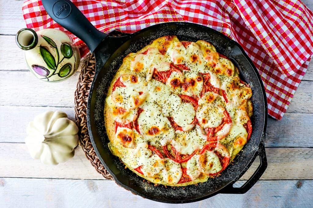 Overhead photo of a pizza in a cast iron skillet with a red and white checked napkin.