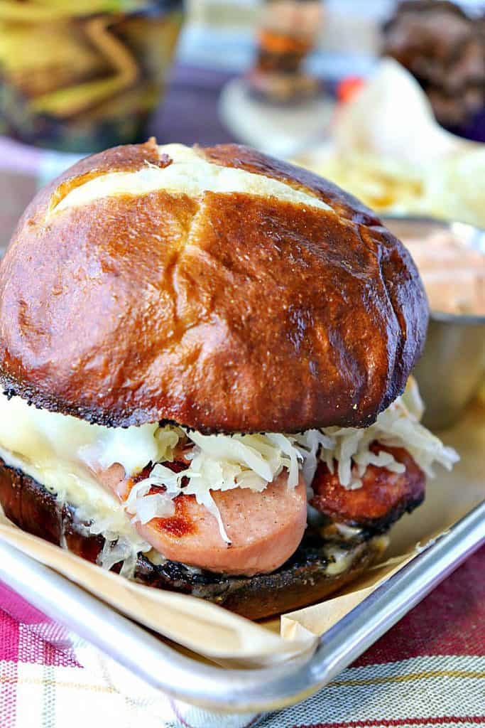 Closeup photo of a knockwurst sausage sandwich with sauerkraut and melted cheese on a pretzel roll.