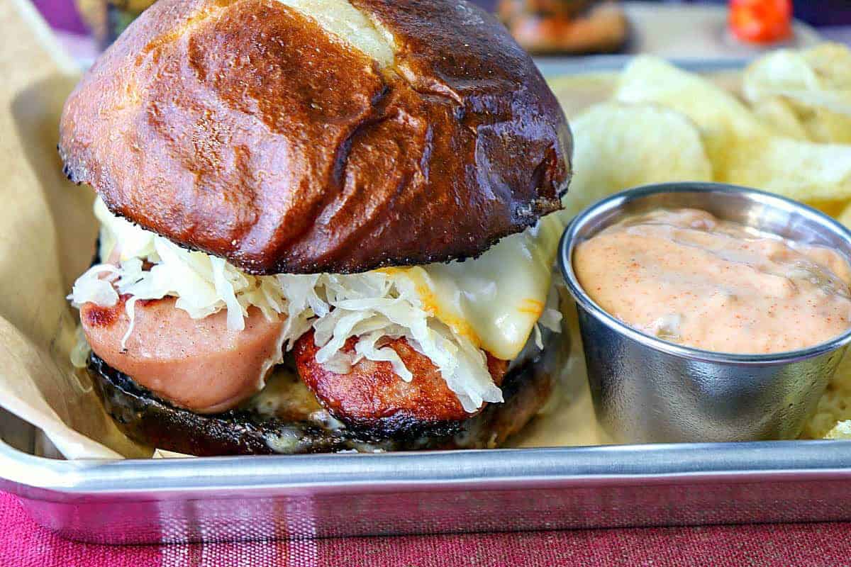 A pretzel roll with sausage, sauerkraut and Muenster cheese sandwich.
