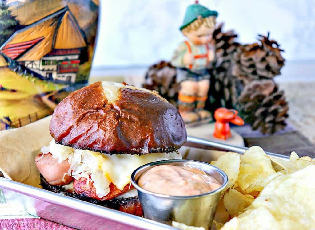 German sausage sandwich on a tray with a German vase in the background with pinecones.