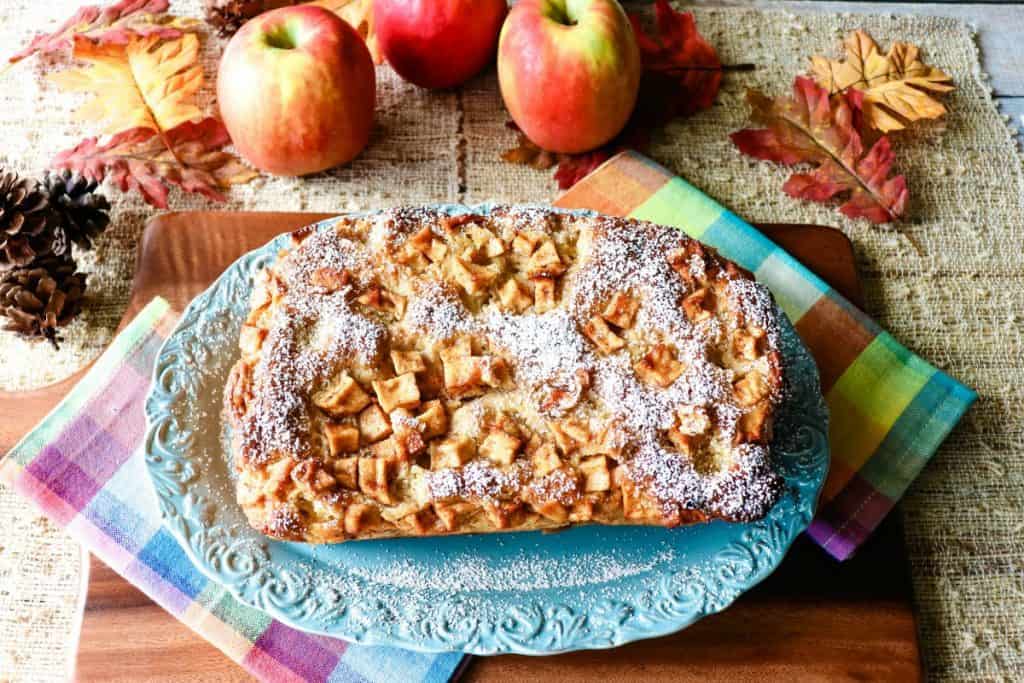 An overhead photo of a loaf of no knead apple yeast bread with colorful napkins and apples in the background.