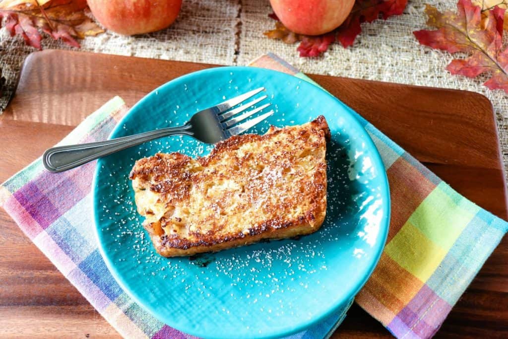 A slice of fried no knead apple yeast bread on a blue plate with a fork and a light dusting of powdered sugar.