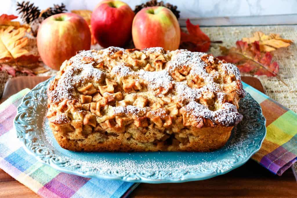 A horizontal photo of a no knead apple yeast bread dusted with confectioners sugar on a pretty blue platter.