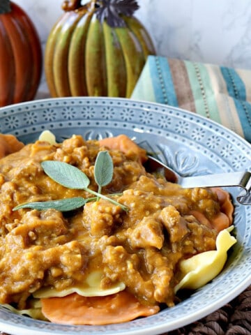 A blue bowl filled with Ravioli with Pumpkin Vodka Sauce and fresh sage on top.