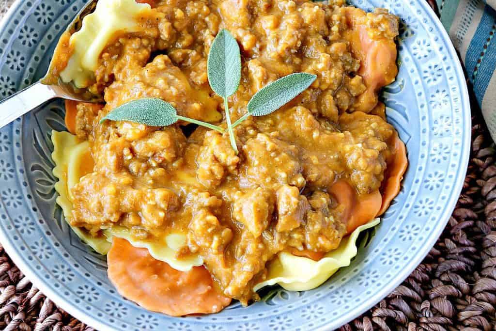 An overhead horizontal photo of Ravioli with Pumpkin Vodka Sauce in a blue bowl with fresh sage as garnish.