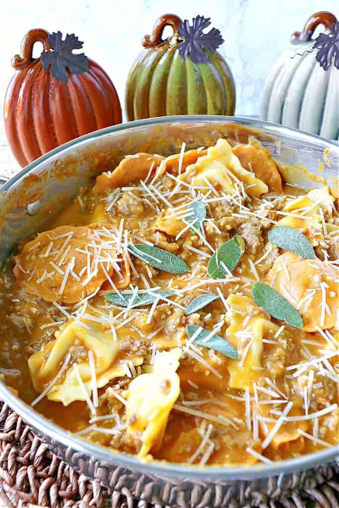 A vertical closeup of a large silver skillet filled with Ravioli with Pumpkin Vodka Sauce, Parmesan cheese, and fresh sage.
