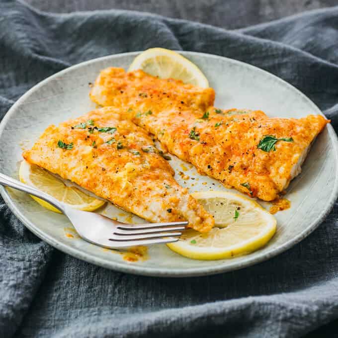 Easy Weeknight Dinner Recipes. Two fish fillets on a plate with lemon slices and seasoning.