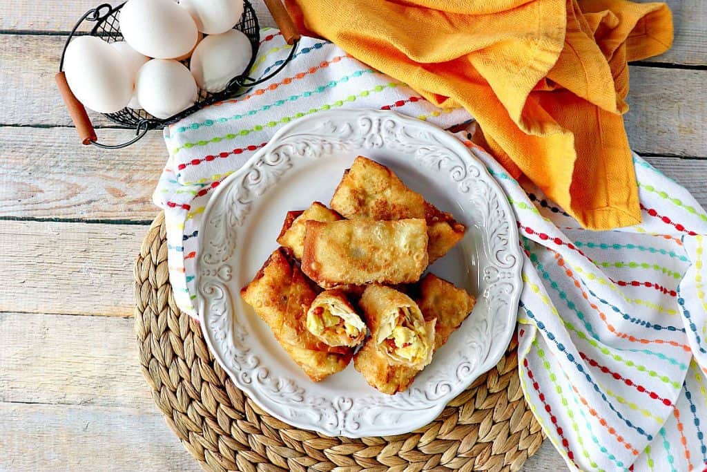 A horizontal photo of Scrambled Egg Rolls on a pretty white plate with a small basket of eggs and colorful napkins.