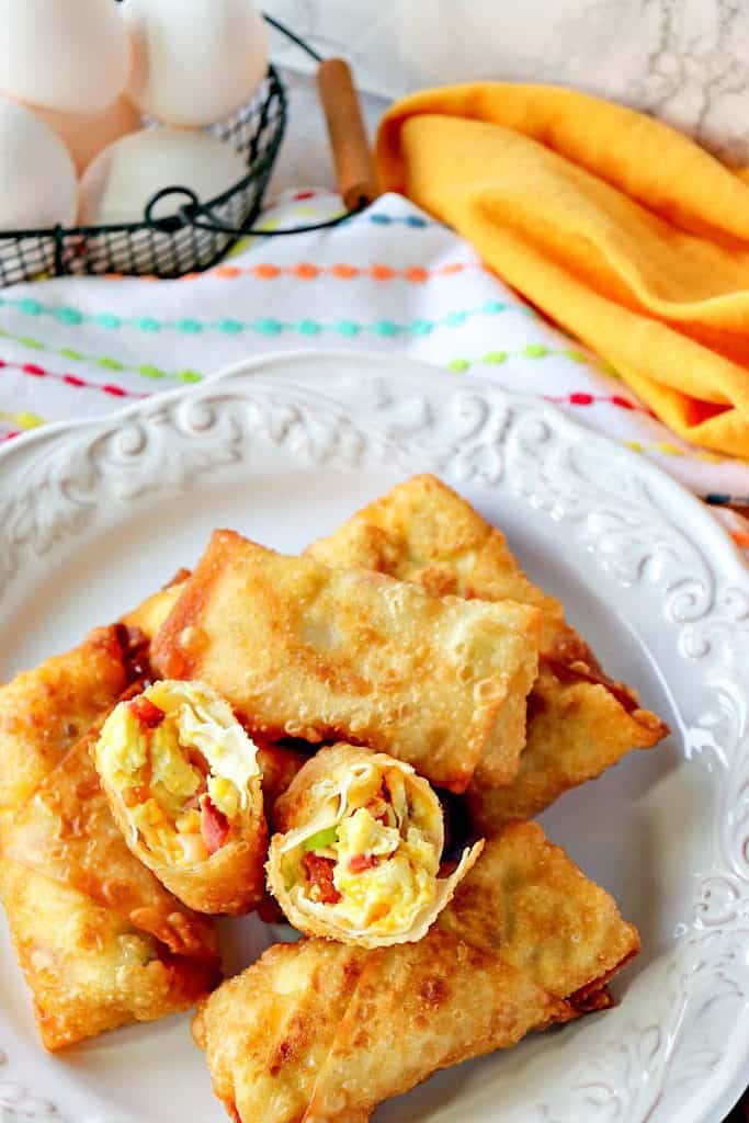 A vertical closeup of a plate filled with breakfast Egg Rolls with colorful napkins in the background and a small basket of eggs.