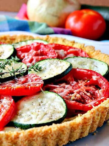 A Tomato Tart with Zucchini along with fresh thyme on top and veggies in the background.