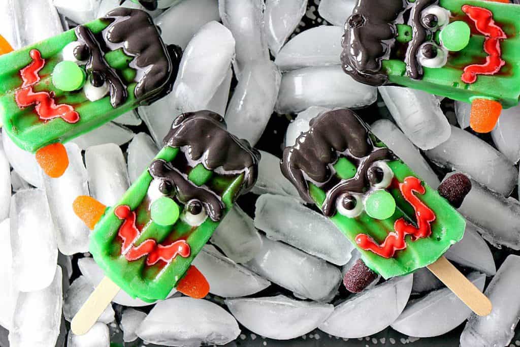 Overhead photo of a tray of ice with frozen Halloween pudding pops with scary faces.